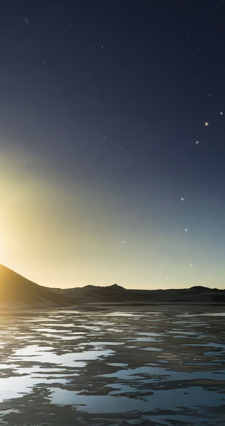First light breaking over a mountain range beneath a star-flecked sky