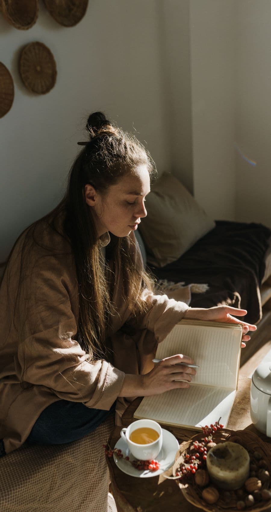 A woman writing in a notebook beside a cup of tea in soft daylight