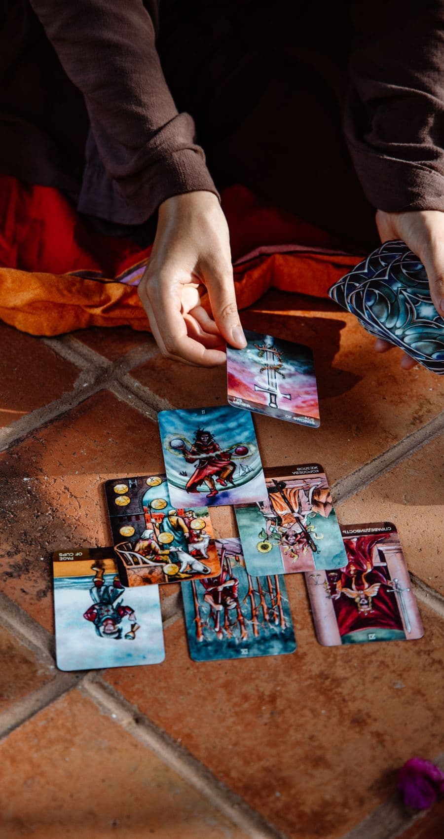 Hands laying out a tarot spread on a warm terracotta cloth