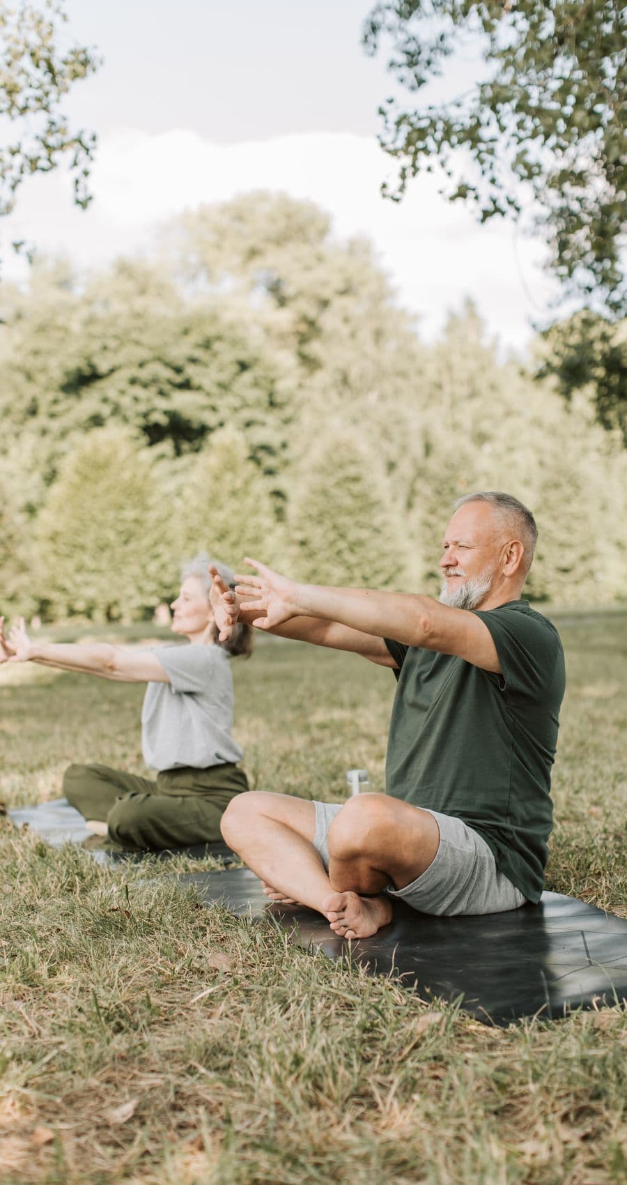 Two people stretching side by side on mats in a sunlit park