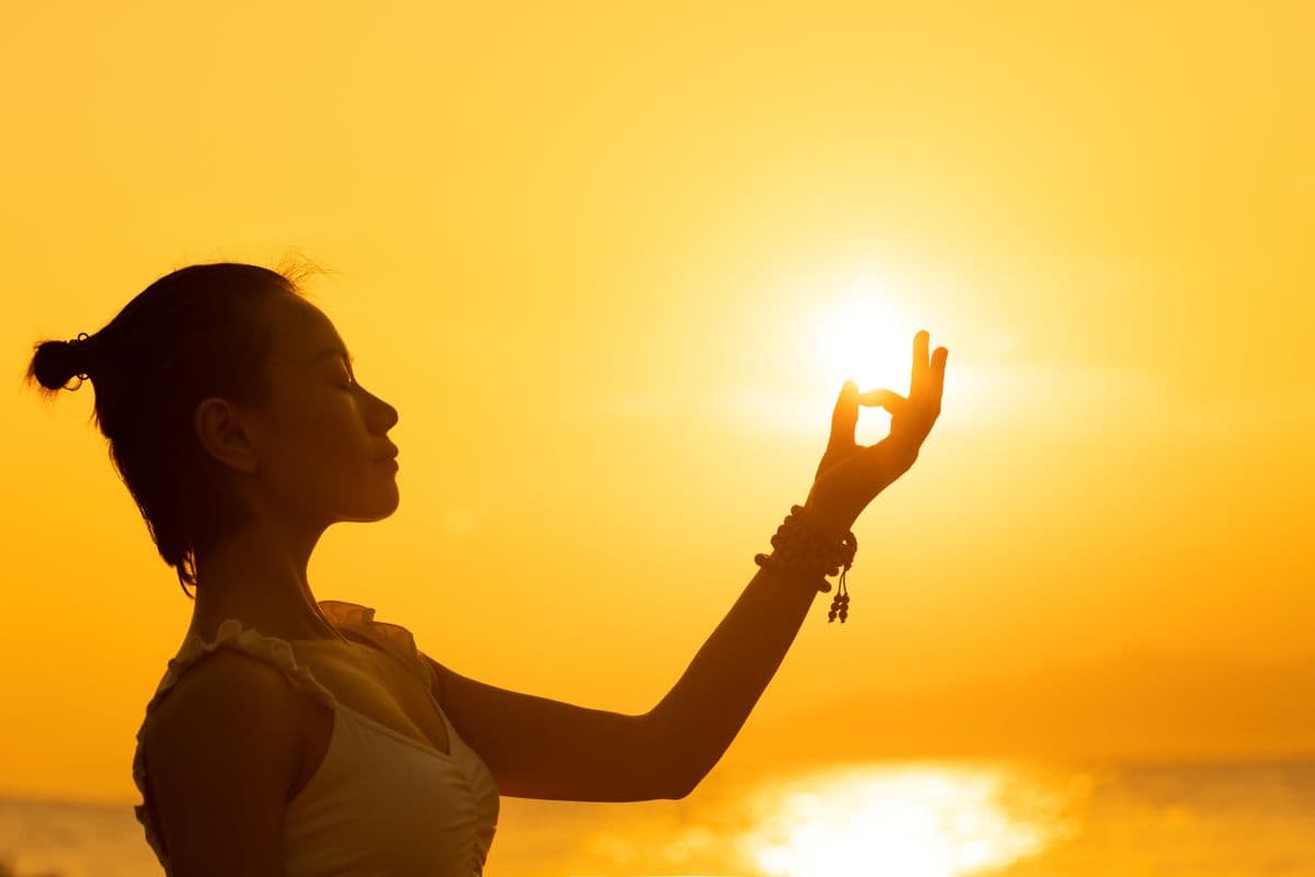 A woman in silhouette cradling the setting sun in meditation