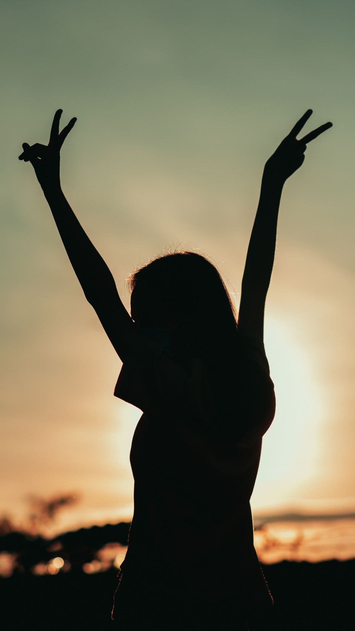 A woman raising her arms toward a glowing sunset in liberation
