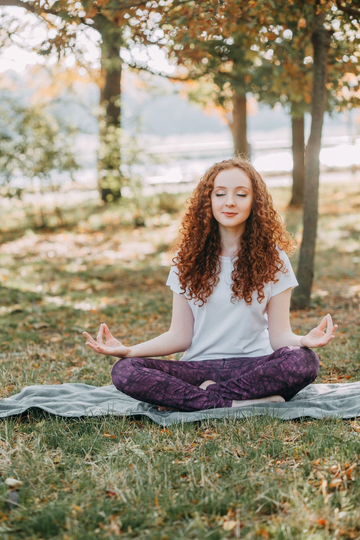 A woman meditating peacefully in lotus pose in a sunlit park